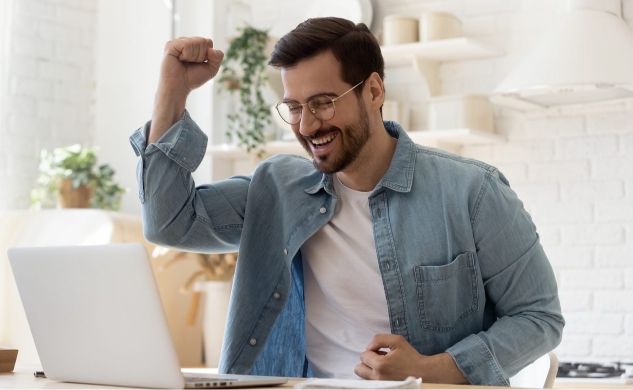 Excited young man on laptop at table celebrating online success