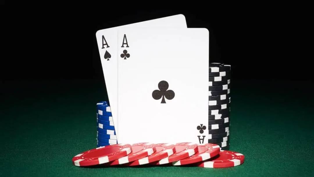 Two aces stand upright on a green casino table with red, blue, and black poker chips around them.