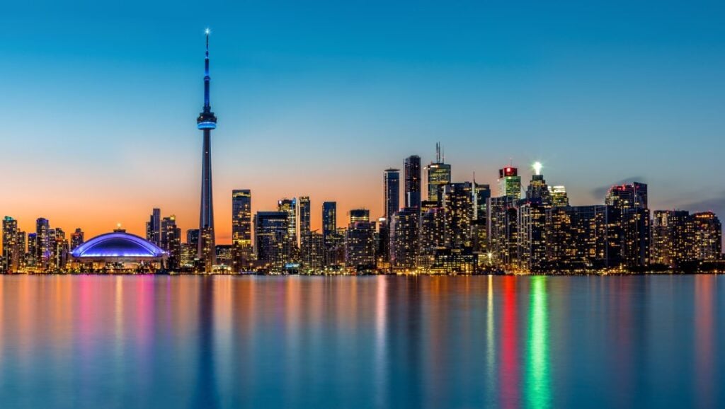 Toronto, Ontario, cityscape view at dusk with a body of water in front of the lit buildings.