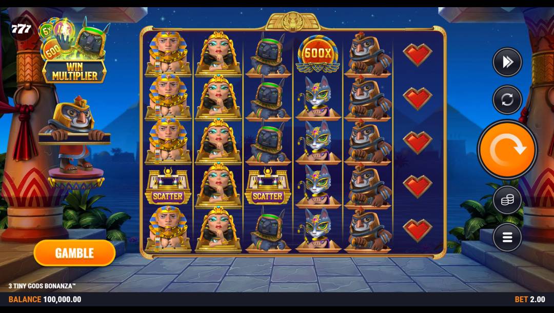 A screenshot of the slot reels in 3 Tiny Gods Bonanza. The backdrop is the view of an Ancient Egyptian city at night with two lit Egyptian columns on the left and right of the screen. The silhouettes of buildings and pyramids are visible against the night sky. In the foreground are the slot reels containing a variety of cute Egyptian-themed symbols, as well as regular slot symbols. Male and female Pharoah, Anubis, Bastet, and Horus symbols, as well as heart, multiplier, and scatter symbols, are visible on the reels.