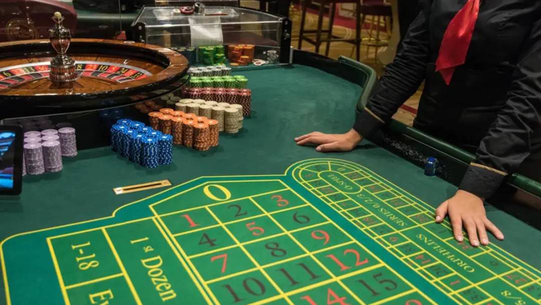 A dealer stands next to a roulette table with their hands on it.
