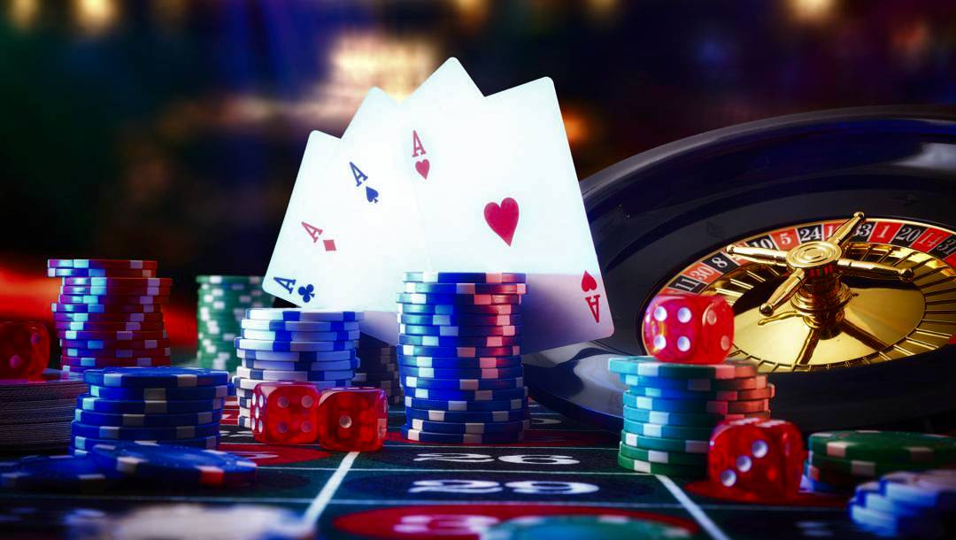 Four aces, poker chips, and dice on a roulette table with a golden roulette wheel in a vibrant casino setting.