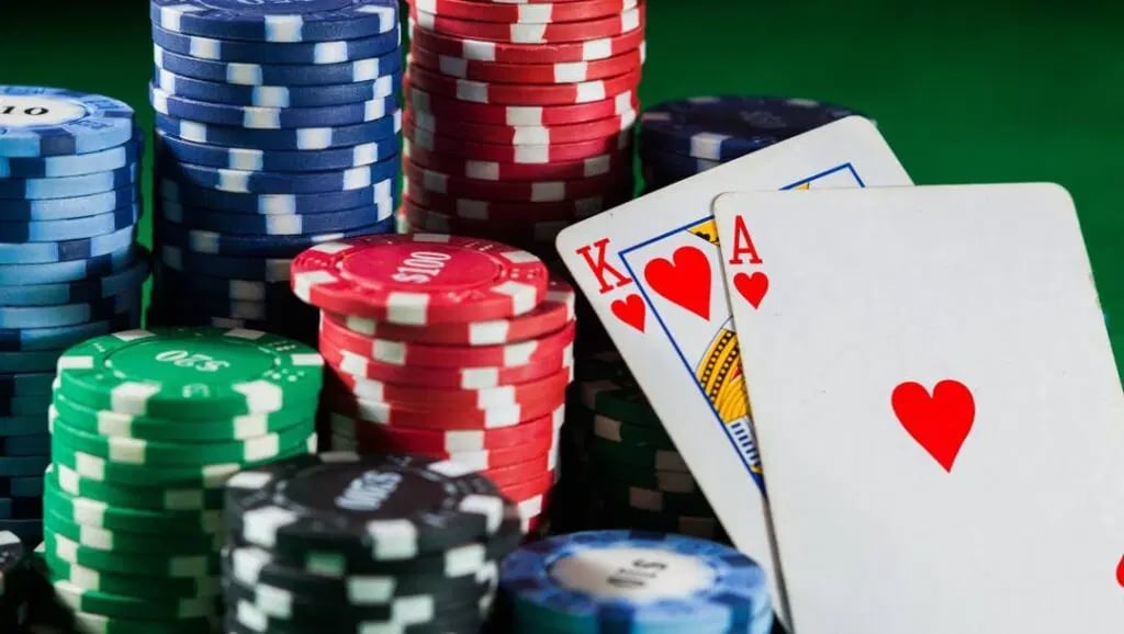 An ace and king of hearts lean against colorful stacks of casino chips on a green table.