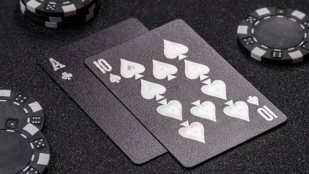 A black and silver ace and 10 on a black table next to black and white casino chips.