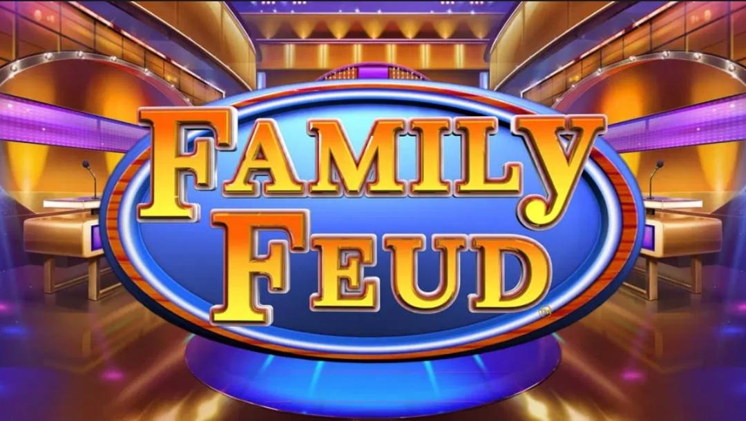 Family Feud slot game logo displayed on a blue oval sign, set within a brightly lit game show studio with podiums and stage lighting.