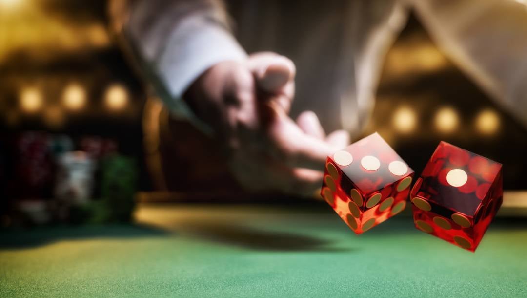 A close-up shot of a person's hand throwing two translucent red dice across a green felt casino game table.