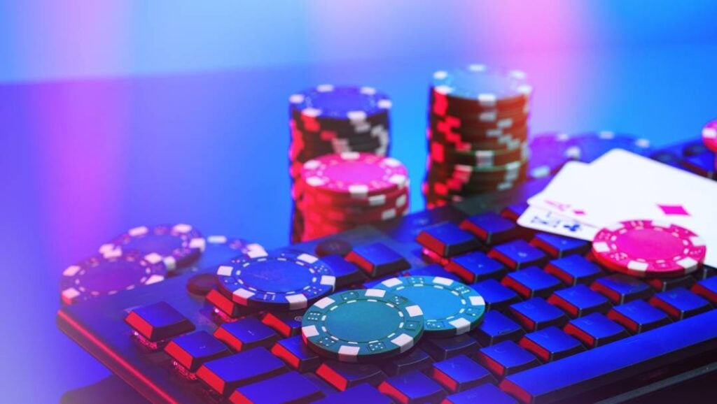 Casino chips and playing cards sit on a computer keyboard under colourful neon lighting.