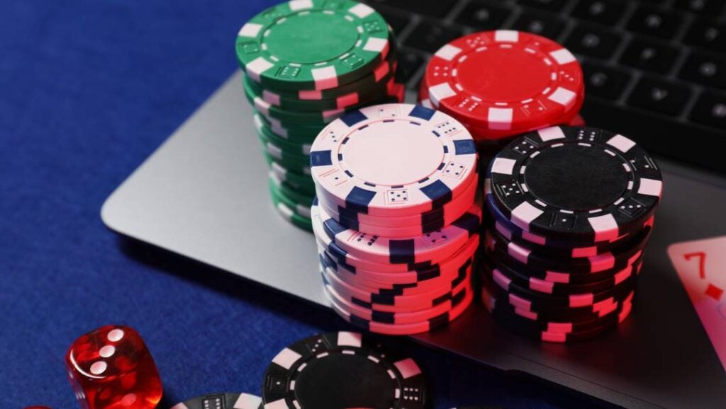 Stacks of colorful poker chips and a red transparent die resting on an open laptop keyboard.